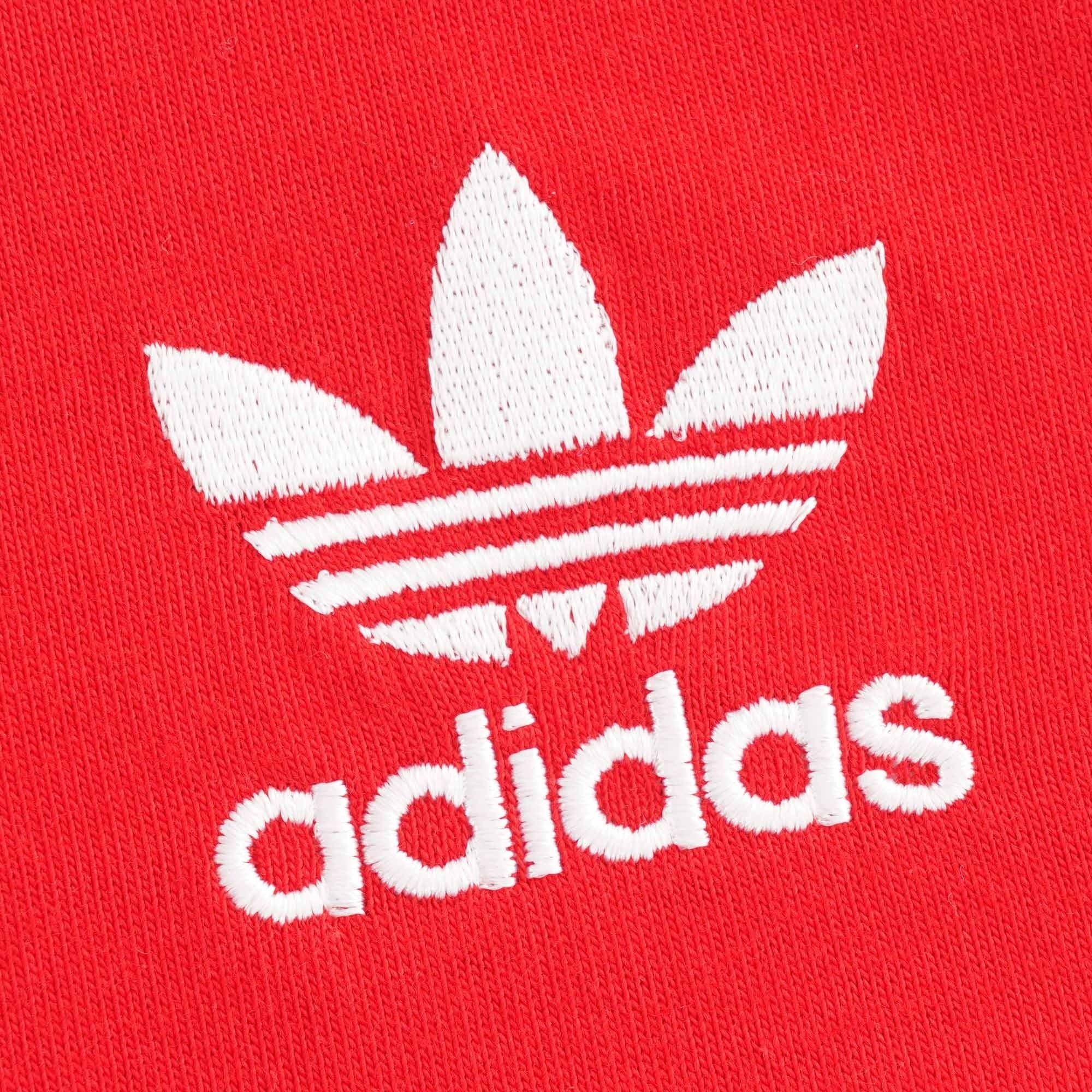 Close-up of the white embroidered Adidas Trefoil logo on the red tee.