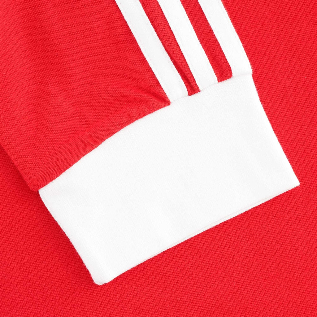 A close-up of a red sleeve with three white stripes and a white cuff.