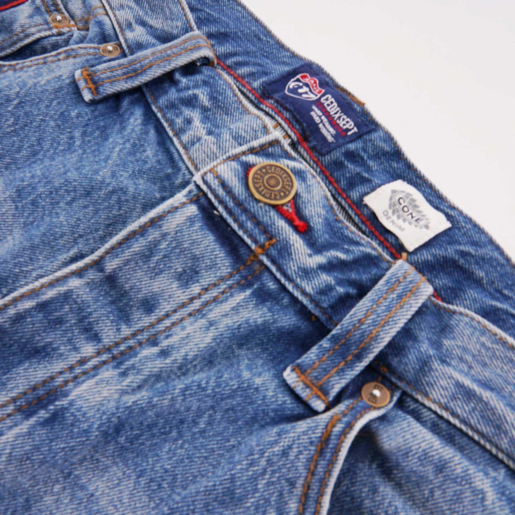 Close-up of the waistband of blue jeans, showing buttons and a brand label.