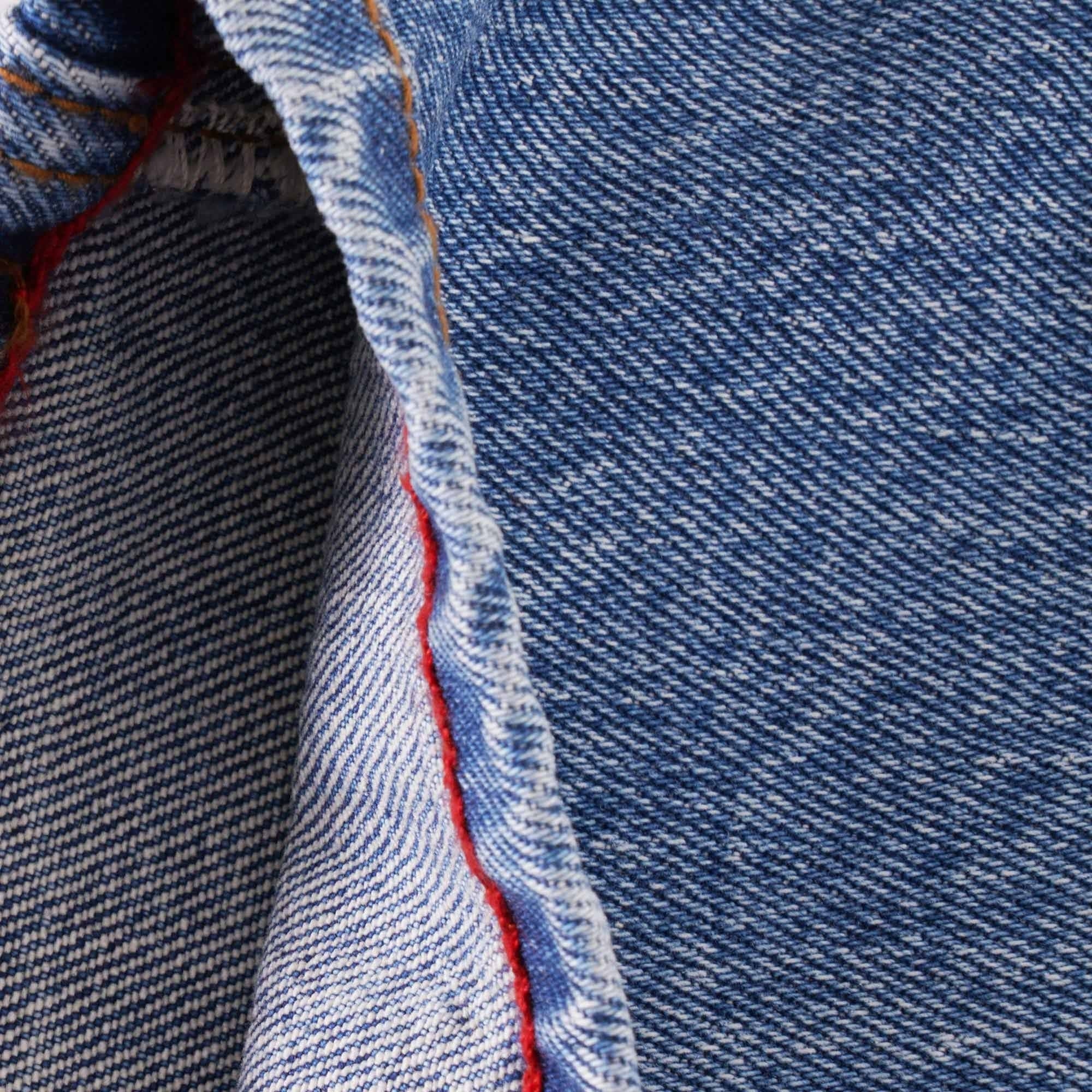 Close-up of the inside seam of blue jeans, revealing red stitching detail.