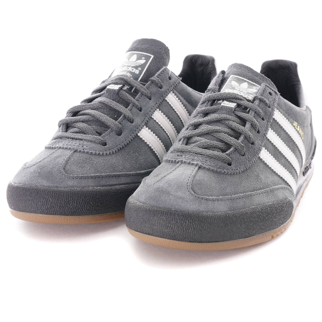 A pair of grey Adidas Jeans trainers with white stripes and brown soles, viewed from the front.