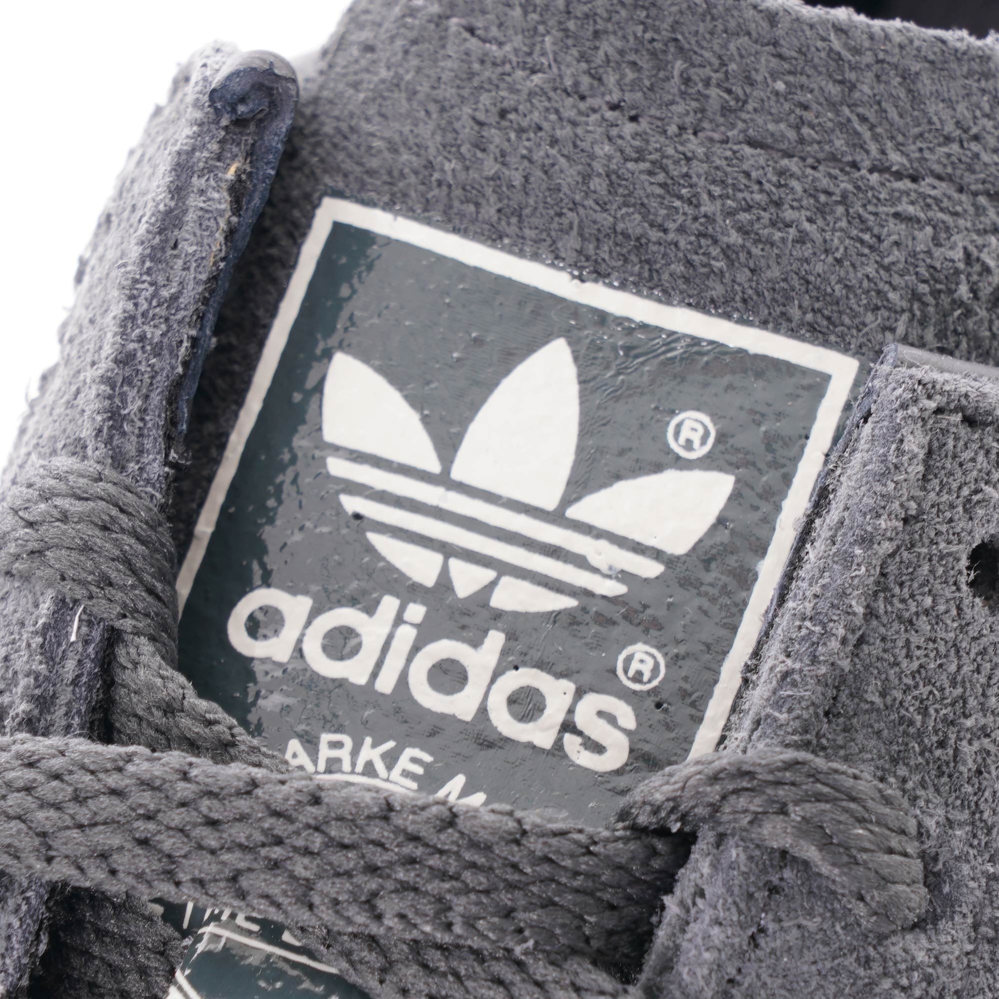 A close-up of the Adidas logo on the tongue of a grey Adidas Jeans trainer.