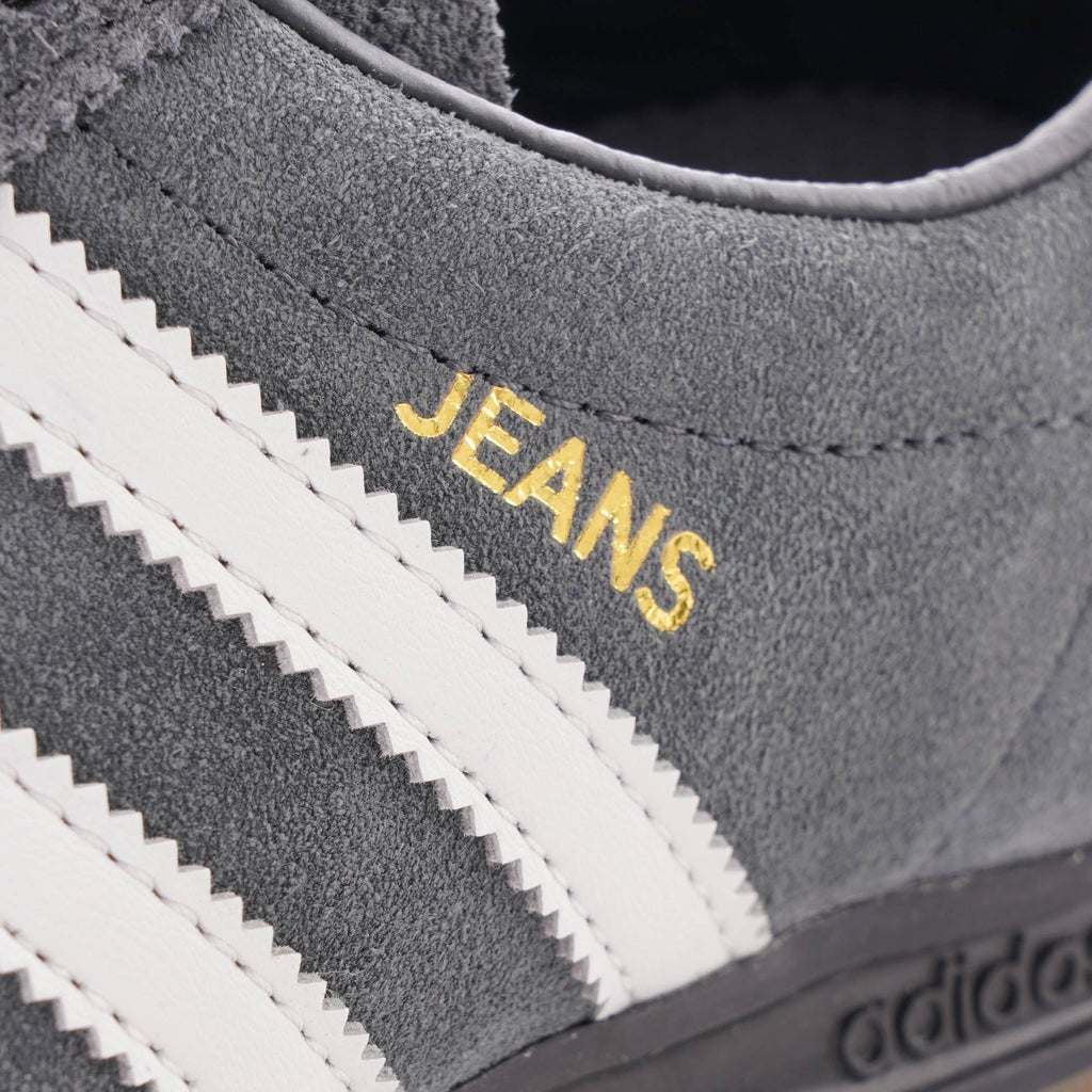 A close-up of the 'JEANS' text in gold lettering on a grey Adidas trainer.