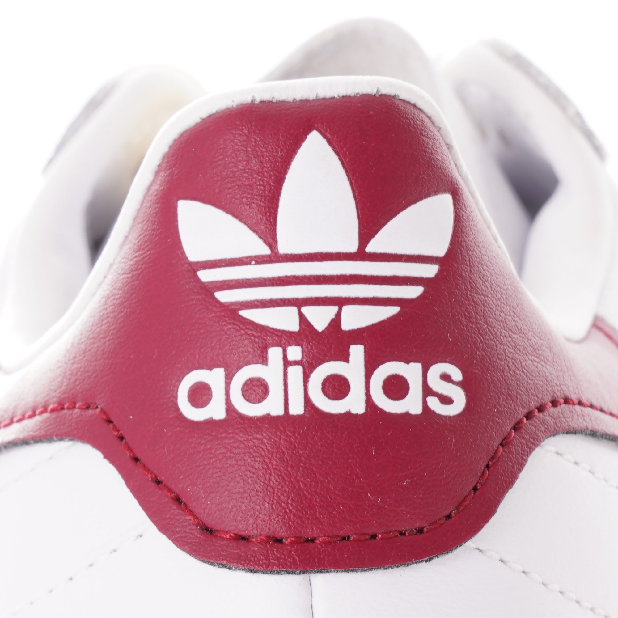 Close-up of the burgundy Adidas logo on the heel of a white trainer.