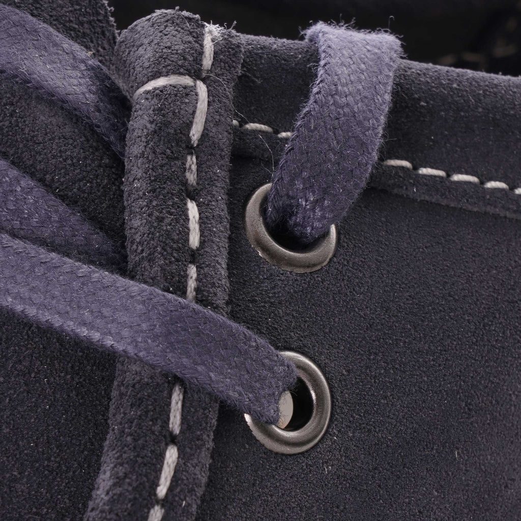 Close-up of the dark blue laces and eyelets on the suede shoe, with white stitching.