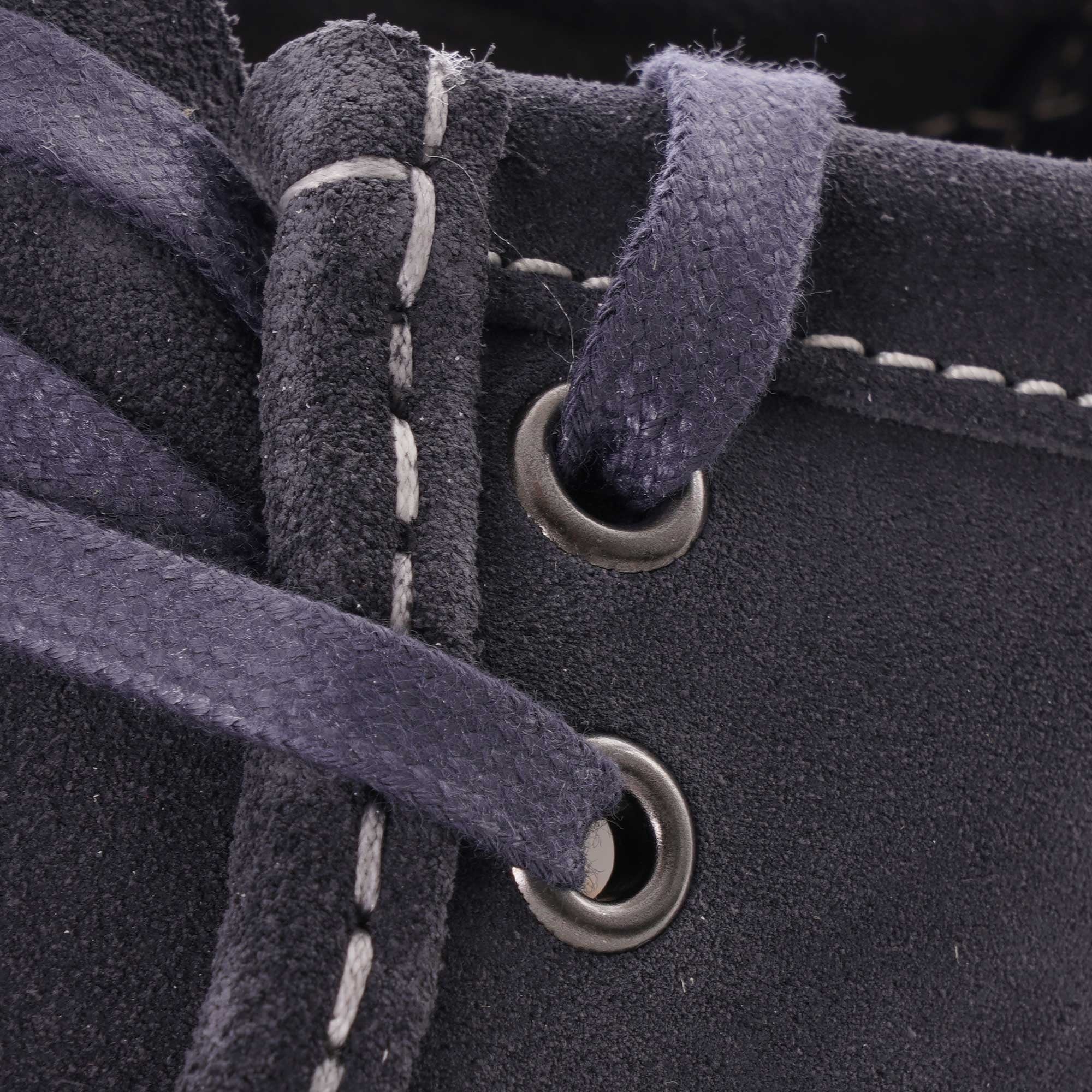 Close-up of the dark blue laces and eyelets on the suede shoe, with white stitching.