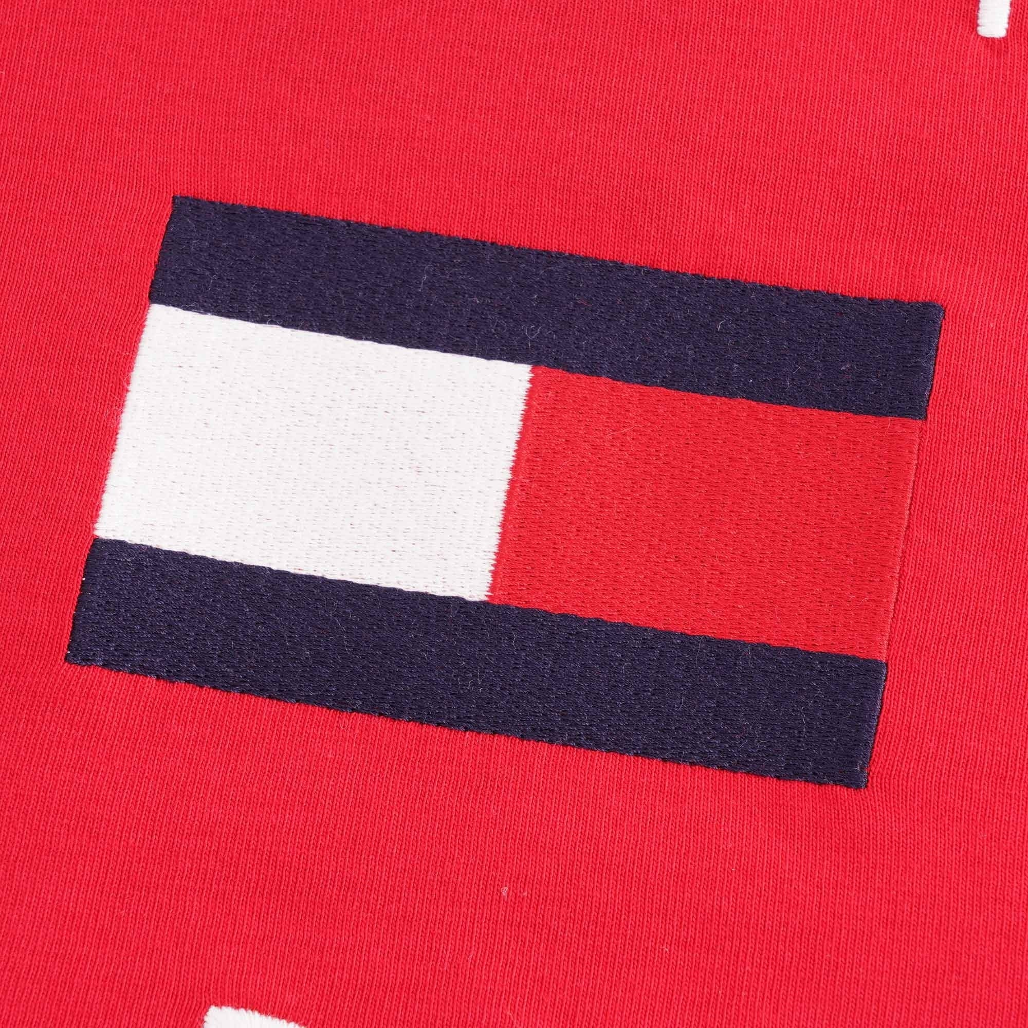 A close-up of the Tommy Hilfiger flag logo embroidered on the red T-shirt.