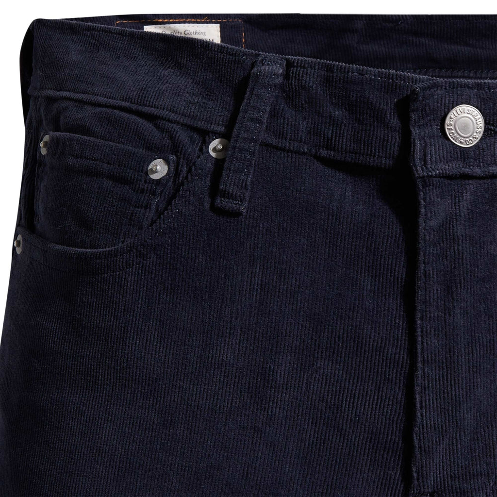 A close-up of the waistband and front pocket detail of navy corduroy trousers.