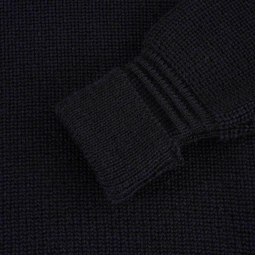 Close-up of the ribbed cuff of a navy blue jumper sleeve.